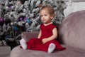 Beautiful cute little girl sitting on the sofa near the New Year tree. Holiday mood, childlike spontaneity and sweet atmosphere Royalty Free Stock Photo