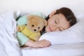 Beautiful cute little girl with a toy teddy bear sleeps in her bed, smiling sweetly Royalty Free Stock Photo