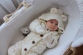 Beautiful 2 month old baby girl in a white knitted suit lies in her white crib