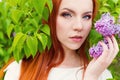 Beautiful cute red-haired girl with long hair in a white dress with a bouquet of lilac in the hands of Royalty Free Stock Photo