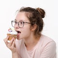 Beautiful cute teen girl with glasses eating cream cake on white background