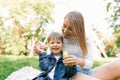 Beautiful cute young mom with her cute little son having fun sitting on the grass in the park outdoors and blowing soap bubbles Royalty Free Stock Photo