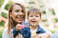 Beautiful cute young mom with her cute little son having fun sitting on the grass in the park outdoors and blowing soap bubbles Royalty Free Stock Photo