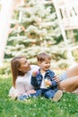 Beautiful cute young mom with her cute little son having fun sitting on the grass in the park outdoors and blowing soap bubbles Royalty Free Stock Photo