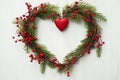 Beautiful cypress Christmas wreath from green twigs red berries in the shape of a heart with ornament on white wood background.