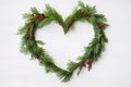 Beautiful cypress Christmas wreath from green twigs red berries in the shape of a heart with ornament on white wood background