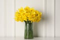Beautiful daffodils in vase on table near white wall indoors