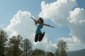 Beautiful dark-haired happy young woman jumping high in air, against background of summer blue sky. horizontal picture Royalty Free Stock Photo