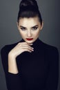 Beautiful dark haired model with perfect make up and her hair scraped back into a high bun leaning her chin on the hand