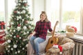 beautiful girl sits near the Christmas tree decorated with balls and light and playing the guitar and singing. Young Royalty Free Stock Photo