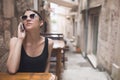 Beautiful dark tan European woman talking on the phone with friend gossiping. Business woman talking phone in the cafe in old town Royalty Free Stock Photo