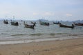 Beautiful day shot of rows of long boats in shallow ocean waters by the shore of yellow sand beach with islands, hills and Royalty Free Stock Photo