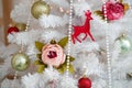 Beautiful decorations are hanging on a white artificial Christmas tree. Green balls, flowers, beads, wooden deer Royalty Free Stock Photo