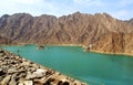 Beautiful deep green Hatta lake with rocky Hajar Mountains on background