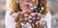 Beautiful defocused woman blow confetti from hands. celebration and event concept. happiness and coloured image. movement and