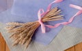 Beautiful delicate bouquet with pink ribbon of dried wheat ears on the table with a purple sheet of paper and a linen napkin