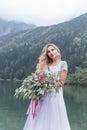 Beautiful delicate girl in the air blue bride wedding dress with luxurious curls in the mountains near the lake with a wedding bou