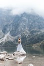 Beautiful delicate girl in the air blue bride wedding dress with luxurious curls in the mountains near the lake with a wedding bou