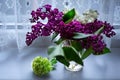 A beautiful, delicate little bouquet of white and lilac flowers in a transparent vase on the window with a white openwork vintage