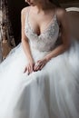 Beautiful delicate bride happy woman with a crown on her head by the window with a large wedding bouquet in a luxurious white