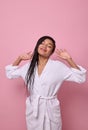 Beautiful delighted African woman wearing white terry bathrobe, stretches her body after waking up, poses with closed eyes against