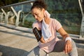 Beautiful delighted female athlete wiping her neck from sweat with white terry towel, sitting on squat position on the city bridge Royalty Free Stock Photo