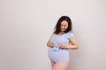 Beautiful delightful smiling pregnant woman holding blue knitted baby booties over her belly, isolated white background Royalty Free Stock Photo