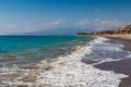 A beautiful deserted sand and pebble beach with foamy waves surf and mountains and a blue sky with white clouds