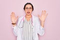 Beautiful doctor woman with blue eyes wearing coat and stethoscope over pink background afraid and terrified with fear expression