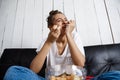 Beautiful domestic girl eating chips, watching tv, sitting at sofa.