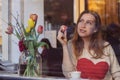 Beautiful dreaming young woman sitting in coffee shop near the window,drining coffee and eating dessert