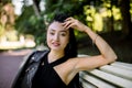 Beautiful dreamy Chinese woman in black trendy clothes, sitting on bench outdoors in the park. Pretty Asian girl sitting Royalty Free Stock Photo