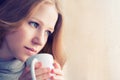 Beautiful dreamy girl with a cup of hot coffee at the window