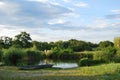 Beautiful, dreamy and quiet landscape with the forest, a pond, a meadow and a blue sky, during a summer day Royalty Free Stock Photo