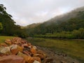 Beautiful early morning view of a creek with reflections of blue sky, foggy mountains and trees on water Royalty Free Stock Photo