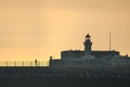 Early morning view of red East Pier lighthouse against epic hazy orange sky with adult running and exercising in Dun Laoghaire