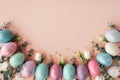 Beautiful Easter border from Easter eggs, flowers and green leaves on pastel background top view. Flat lay