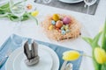 Beautiful Easter table setting with festive decor indoors. Napkin in shape of rabbit ears, colorful eggs in nest, fresh yellow Royalty Free Stock Photo