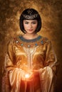 Beautiful Egyptian woman like Cleopatra with magic ball on golden background