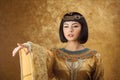 Beautiful Egyptian woman like Cleopatra pointing finger away on golden background