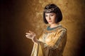 Beautiful Egyptian woman like Cleopatra pointing finger away on golden background