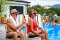 Beautiful elderly couple enjoying hot day outdoors by pool with friends, putting sunscreen on. Group of cheerful seniors Royalty Free Stock Photo