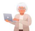 Beautiful elderly woman in glasses works at a laptop. Old gray-haired grandmother holds a personal computer in her hand