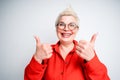 A beautiful elderly woman in a red shirt and glasses smiles and thumbs up. Isolated on light background Royalty Free Stock Photo