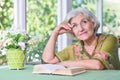 Beautiful elderly woman sits at a table and reading book Royalty Free Stock Photo