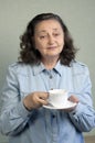 A beautiful elderly woman about 65 years old rejoices, smiles. In the hands of a cup of tea or coffee Royalty Free Stock Photo
