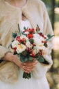 Beautiful elegant autumn wedding bouquet of white roses and red flowers in the hands of the bride in in beige fur coat Royalty Free Stock Photo