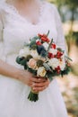 Beautiful elegant autumn wedding bouquet of white roses and red flowers in the hands of the bride in white wedding dress Royalty Free Stock Photo