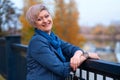 Beautiful elegant blond woman posing in autumn city park, dressed in blue jeans and jacket Royalty Free Stock Photo