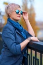 Beautiful elegant blond woman posing in autumn city park, dressed in blue jeans and jacket Royalty Free Stock Photo